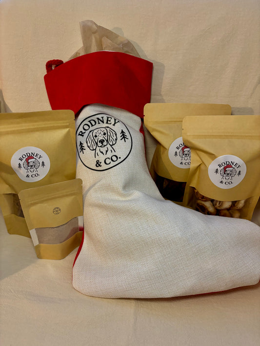 Red and white linen Christmas stocking printed with the Rodney & Co. dog logo, surrounded by bags of dog treats